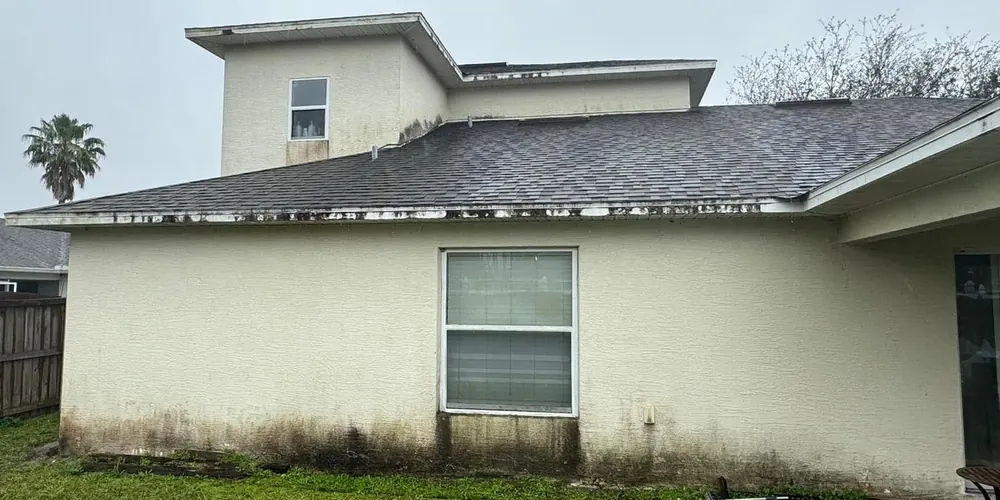 Before: two-story stucco home with mildew along the walls