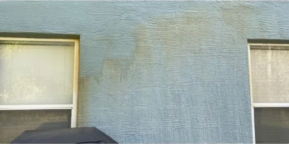 Before: rust stains on a stucco wall between windows
